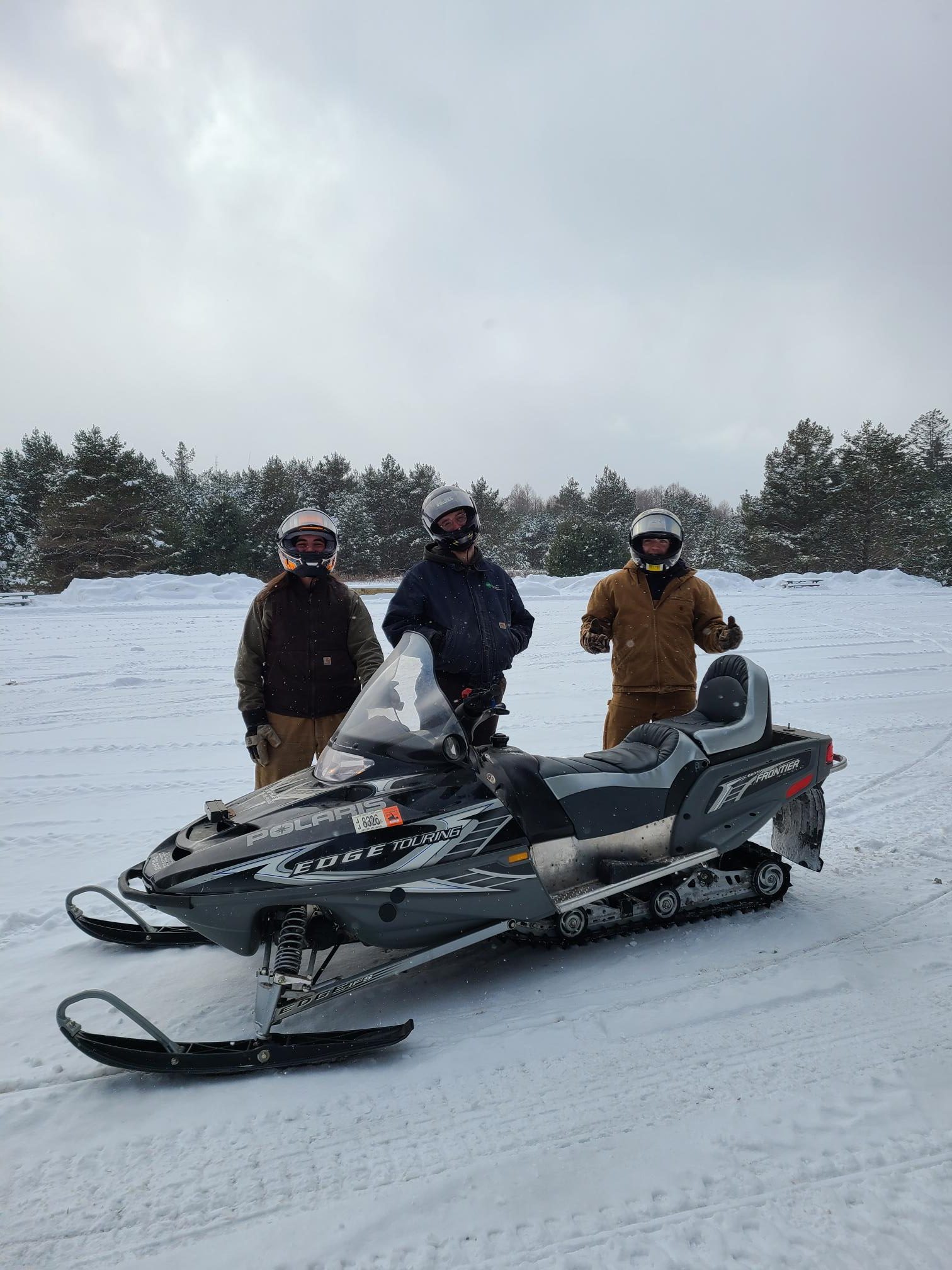 snowmobile with 3 people standing behind in helmets and winter gear