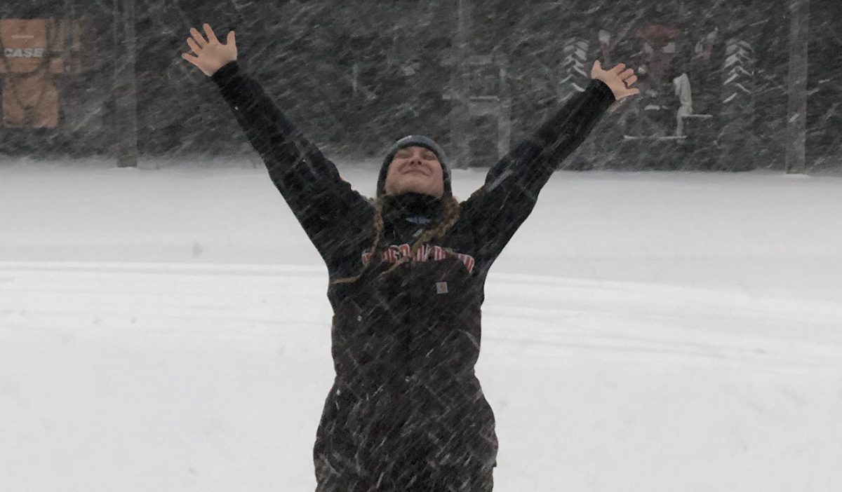 Crew member standing in snow with arms up looking skyward
