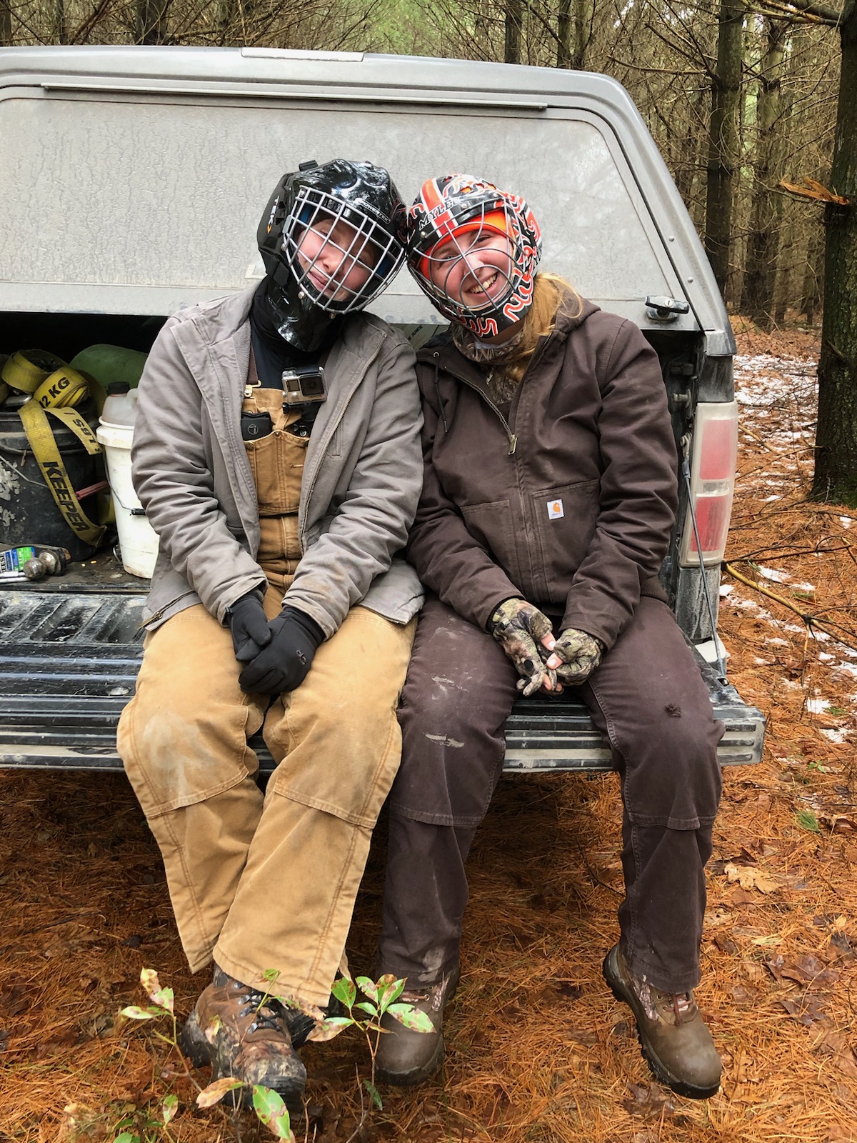 2 crew members sitting on the tail gate in field gear and goalie helmets