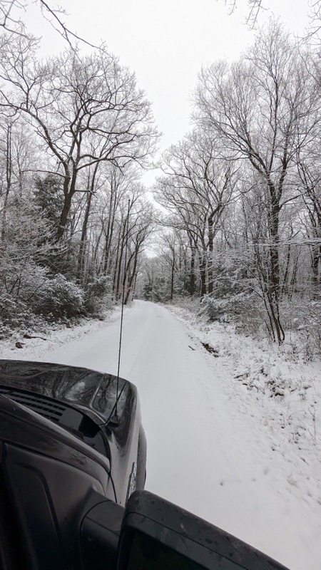 View of snow covered forest road from over a truck hood